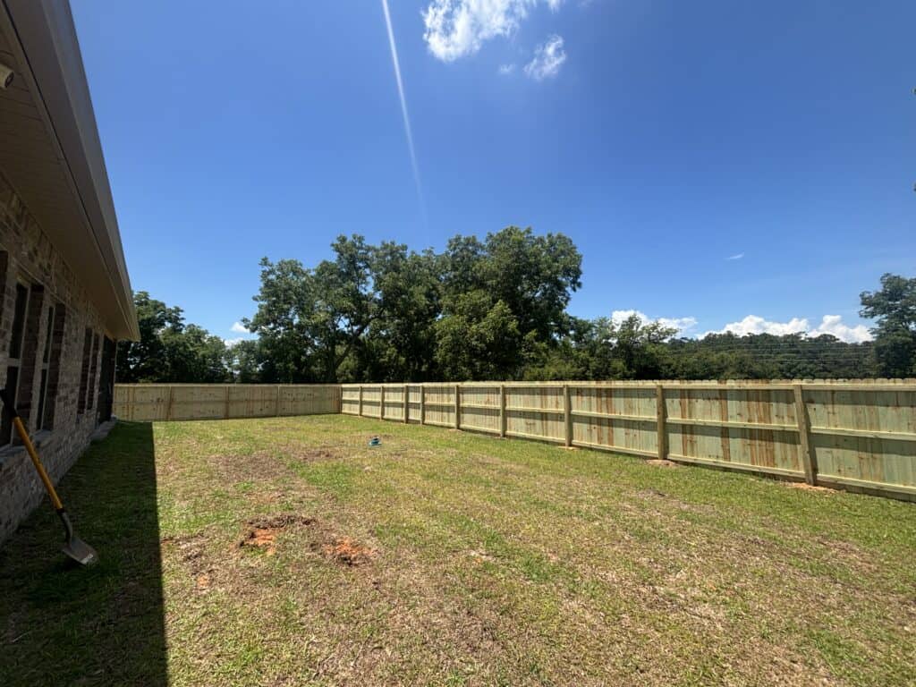 New wood privacy fence enclosing a freshly landscaped backyard beside a home.